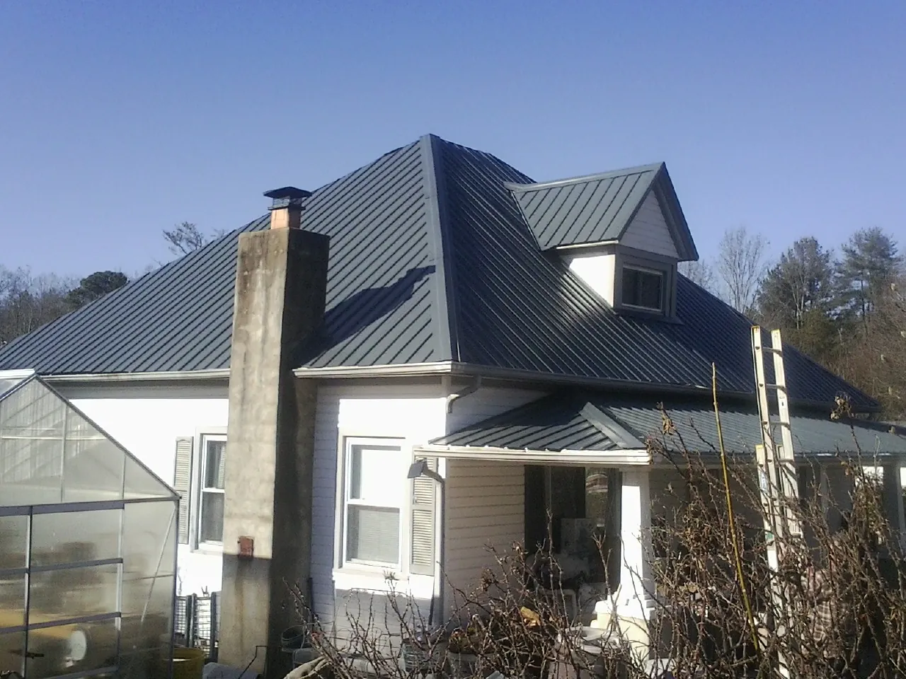 Dark blue standing seam metal roof on a white farmhouse with dormer — Slate & Tile Roof Repair by Roofing Brothers in Crane
