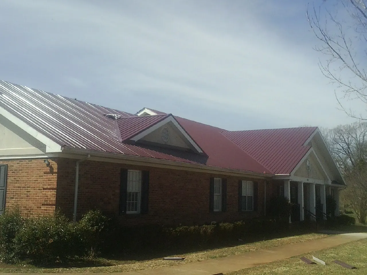 Red metal roof with gabled entries on a long brick building, from a Hail Damage Roof Repair job in Crane
