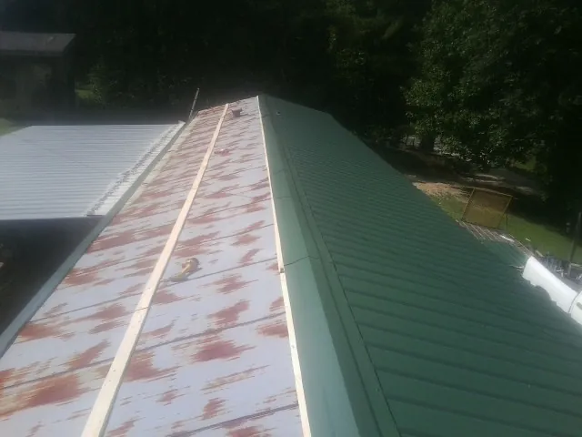 Old rusted panels beside newly installed green metal roofing — Wind Damage Roof Repair by Roofing Brothers in Crane