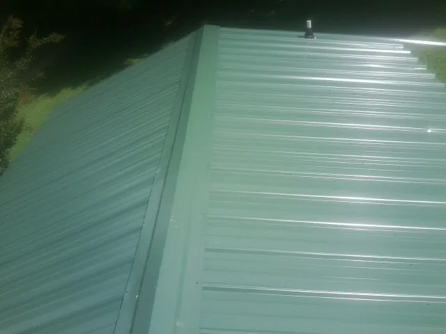 New green metal panels meeting at the ridge of a roof — Flat Roof Repair work by our crew in Crane
