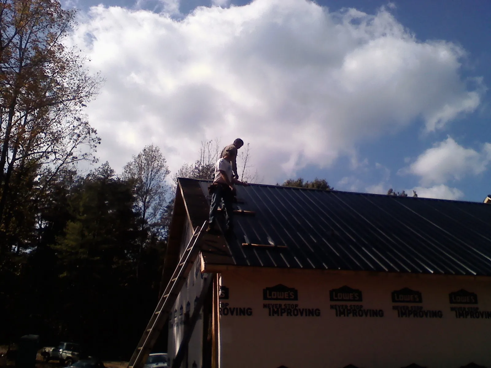 Roofer fastening dark metal panels high against a cloudy sky, from a Roof Inspection job in Crane