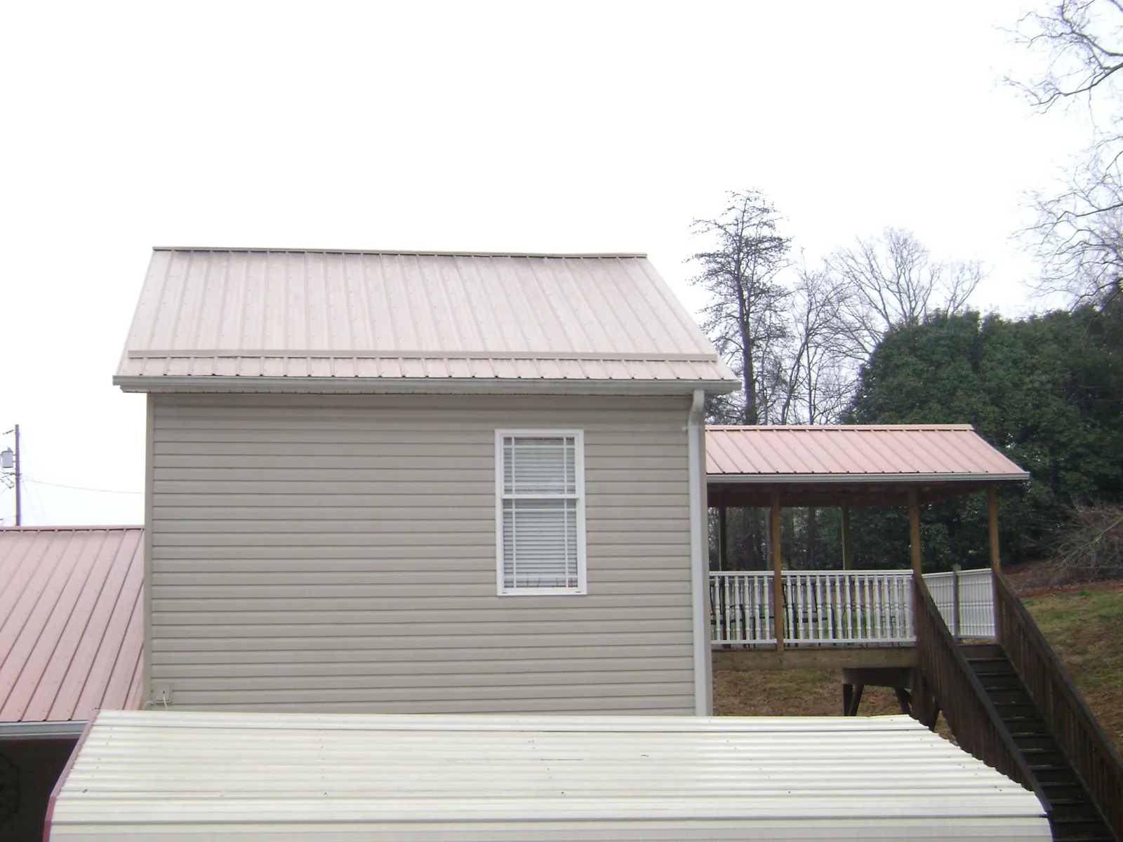 Tan metal roofs on a two story addition and attached porch, from a Roof Replacement job in Crane